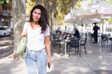  woman with shoulder bag walking near outdoor cafe.