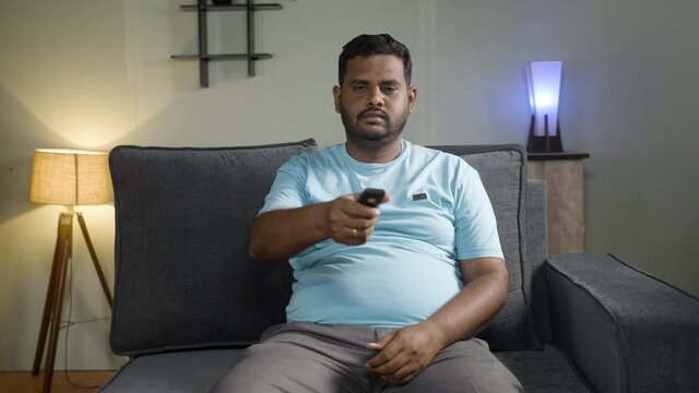 Obese Indian fat man watching tv during weekend at home - concept of boredom, laziness and relaxation or leisure activities.