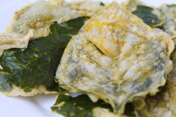 Deep fried green amaranth leaves or spinach leaves, cover with flour dough, on a white plate.