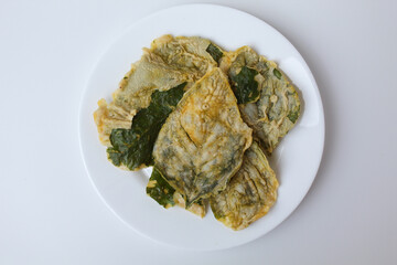 Deep fried green amaranth leaves or spinach leaves, cover with flour dough, on a white plate. Isolated on white background. Flat lay or top view.