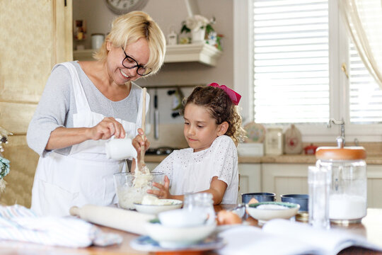 Image of a grandmother and cute adorable granddaughter prepare together in the kitchen, with ingredients on the table.