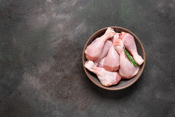 Raw chicken drumstick in a bowl on a dark grunge background. Top view, copy space.