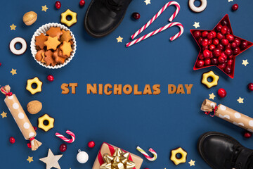 Christmas card with children's shoes, sweets, candy, gingerbread cookies, gifts on blue background, top view.   Saint Nicholas Day, 6 December.