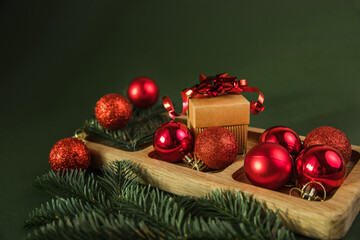 Fototapeta na wymiar Top view of festive wood plate with red baubles, Christmas tree and gifts on green background. Christmas decorations and toys. New Year advent concept. Close-up