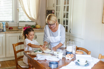 Obraz na płótnie Canvas Grandmother and cute little granddaughter in the kitchen, they are preparing together homemade cookies.