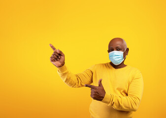 Senior black man in protective face mask pointing at copy space for text or advertisement over...