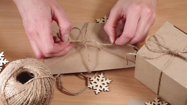 Hands are wrapping gifts in an environmentally friendly style, Full HD. Homemade gifts, DIY. Hands tie a twine bow on an envelope