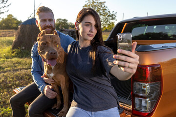 It is selfie time for this young couple and their dog while they are sitting on the back of a...