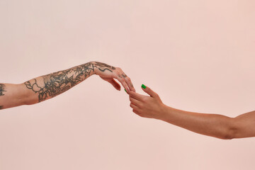 Closeup of two female arms reaching each other hand isolated over light pink background