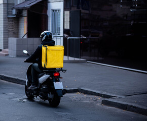 Delivery of food from cafes and restaurants, a courier on a scooter with a yellow backpack travels around the city. Fast food delivery to customers.