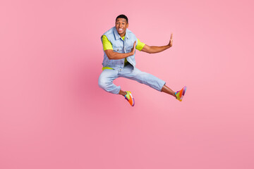 Fototapeta na wymiar Full size photo of crazy young guy jump wear vest t-shirt jeans sneakers isolated on pink background