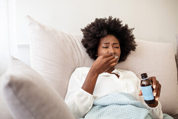 Sad sick young woman in blanket pouring antipyretic or cough syrup from bottle to spoon at home....