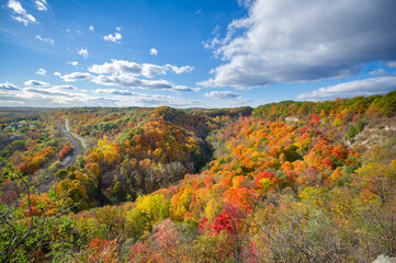 Beautiful Autumn colours views of the Spencer Gorge along the Dundas Peak trail in Hamilton, Ontario, Canada. Train tracks are visible from the lookout. Clouds are present on the blue sky.