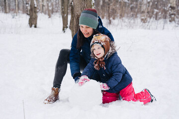 Fototapeta na wymiar Children play outdoors in snow. Outdoor fun for family Christmas vacation. Two little kid boy and girl in funny hats playing outdoors. Happy siblings having fun with snowman