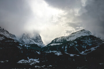 intense mood mountain range in switzerland alps, strong clouds and bright light at midday