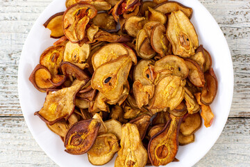 A pile of dried pears in slices on a white plate on wooden background. Dried fruit chips. Healthy food