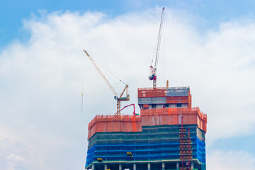 Fototapeta premium Operated tower construction cranes on the roof top of skyscraper against the blue sky background. Industrial background construction.