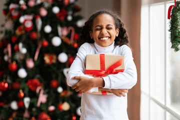 Happy black girl celebrating Christmas hugging gift box