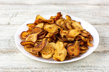 A pile of dried pears in slices on a white plate on wooden background. Dried fruit chips. Healthy food