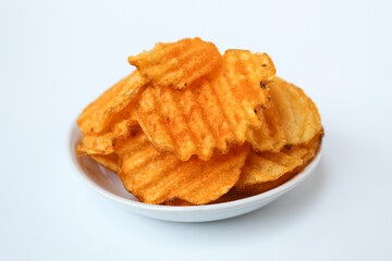 Wavy potato chips, with red powder seasoning, on a small plate. Isolated on white background.