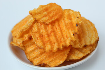 Wavy potato chips, with red powder seasoning, on a small plate. Isolated on white background.