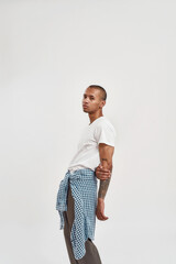 Stylish young mixed race tattooed guy in hip hop casual outfit posing for camera, standing isolated...