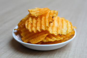Wavy potato chips, with red powder seasoning, on a small plate. Wooden background.