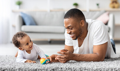 Father-infant bonding. Happy young black dad playing with baby son at home