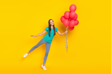 Fototapeta na wymiar Photo of inspired funny lady hold balloons dance wear teal t-shirt jeans sneakers isolated yellow color background