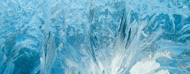 Frosty patterns on glass. Christmas background. Ice on winter window. Abstract crystals close up.