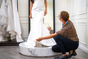 Asian LGBTQ guy bridal shop owner helping female bride customer choosing and trying on wedding gown at wedding studio. Small business entrepreneur wedding planner and marriage ceremony concept