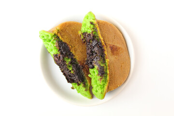 Green colored pukis with melted chocolate topping. Pukis is an Indonesian traditional sweet pancake. On a small white plate. Isolated on white background. Flat lay or top view