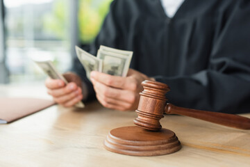 selective focus of gavel near cropped judge counting dollars on blurred background, anti-corruption...