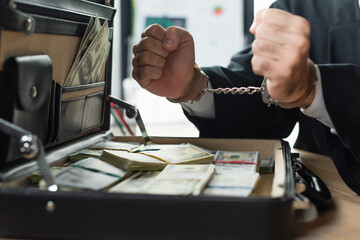 partial view of handcuffed businessman near blurred briefcase with dollars, anti-corruption concept