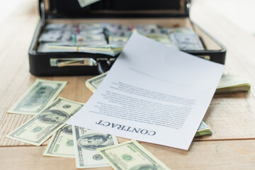 Obraz premium contract near dollar banknotes and blurred briefcase with money, anti-corruption concept