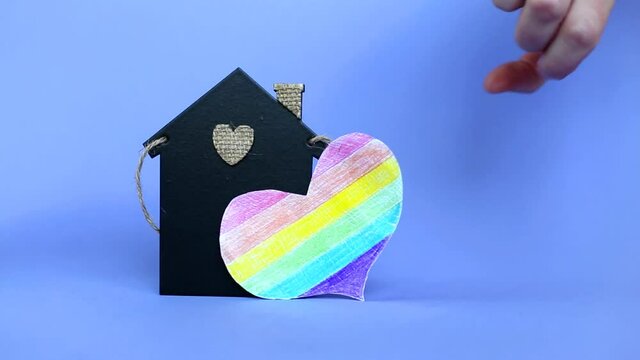 heart in the form of a lgbt flag next to a miniature toy house