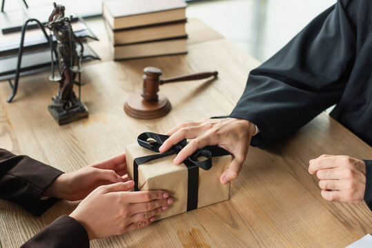 cropped view of judge taking gift from client near blurred gavel on desk, anti-corruption concept