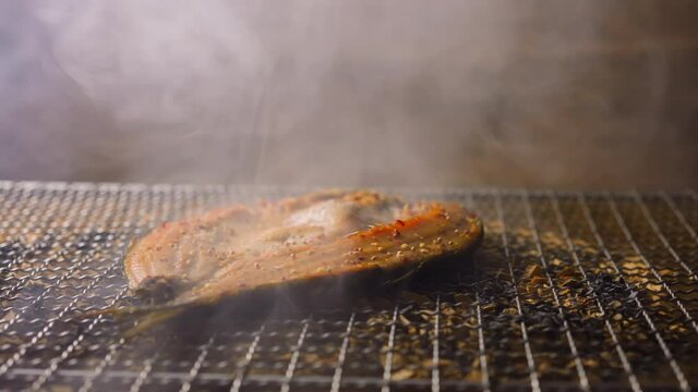 Smoking delicious fresh ide fish steak with rising up hot steam on metal grid lying on pile of wooden chips and charcoals closeup slow motion