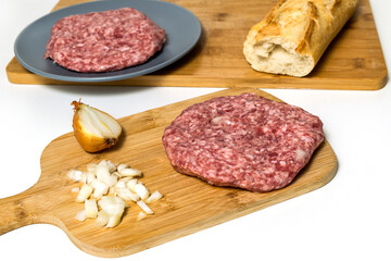 Raw minced meat burgers with onion and spices on white table or board for background. Selective focus. Raw meat hamburger with fresh onion on a wooden board ready to fry