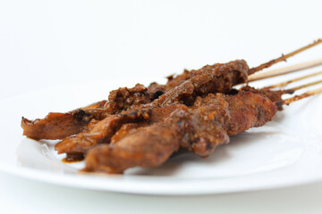 Chicken satay covered by peanut sauce, with bamboo skewers. Indonesian traditional food. On a white plate. Isolated on white background