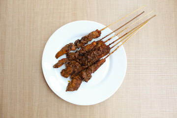 Chicken satay covered by peanut sauce, with bamboo skewers. Indonesian traditional food. On a white plate. Isolated on white background. Flat lay or top view