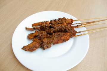 Chicken satay covered by peanut sauce, with bamboo skewers. Indonesian traditional food. On a white plate. Isolated on white background