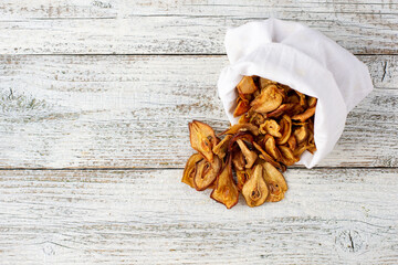 A pile of dried slices of pears pills out of a white pouch on wooden background. Dried fruit chips. Healthy food