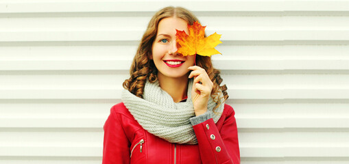 Portrait of beautiful young woman covering her eyes with yellow maple leaves wearing a red jacket, scarf on white background