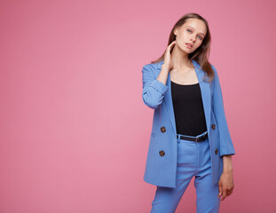 Fashion photo of a beautiful elegant young woman in a pretty blue suit, jacket, pants, trousers posing over pink background. Studio shot, portrait. Pink and blue colors