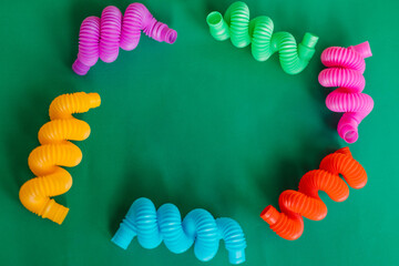 Colorful anti-stress fidget pop tube sensory toy on green background. Flat lay.