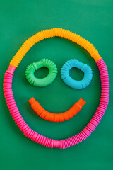 Colorful anti-stress fidget pop tube sensory toy on green background. Smile. Flat lay.