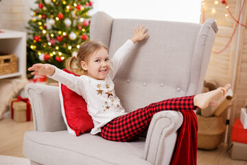 Little girl have fun on armchair in christmas decorated room