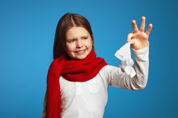 Young kid being disgusted for the tissue she is holding up, isolated over blue background 