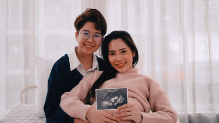 Pregnant Asian lesbian woman and her partner are happy to spend time together at home. - obrazy, fototapety, plakaty